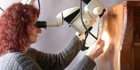 A restorer views a piece of furniture through a scope